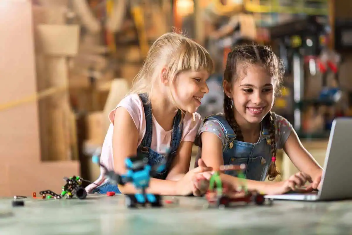 Two girls engaged with a laptop in a garage workshop, surrounded by robotics and craft supplies, exemplifying innovative homeschool room ideas.