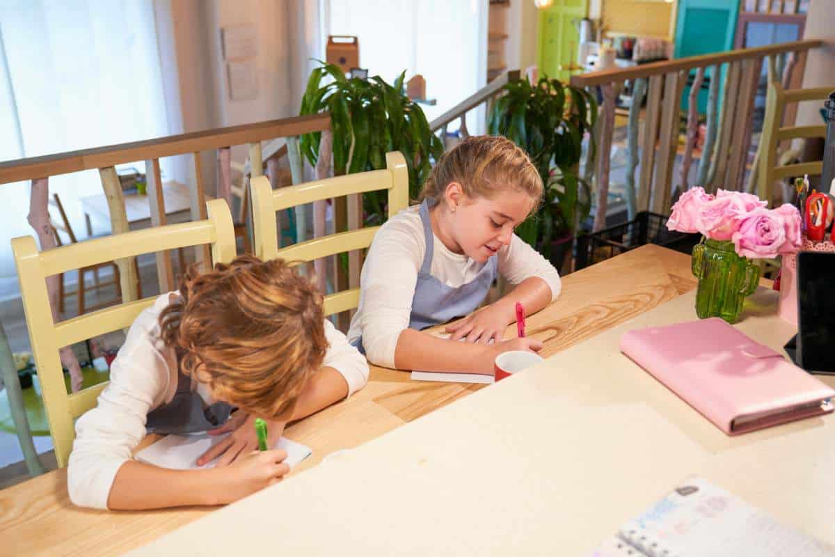 Two children focused on their drawing tasks at a wooden table, part of a creative homeschooling setup on a landing, offering unique homeschool room ideas.