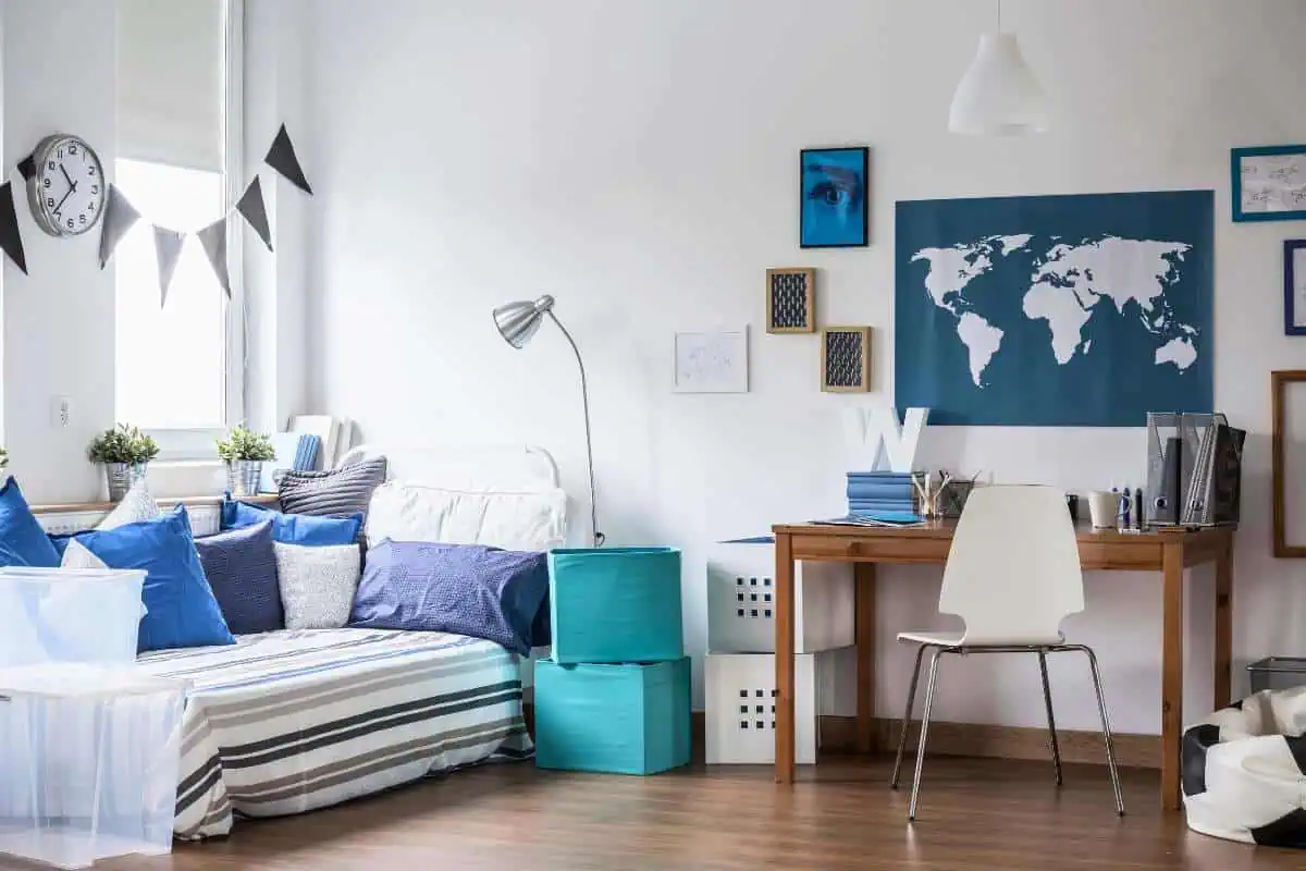 Cozy homeschool bedroom with a daybed adorned with blue pillows, a study desk, and a world map on the wall, ideal for creative homeschool room ideas.