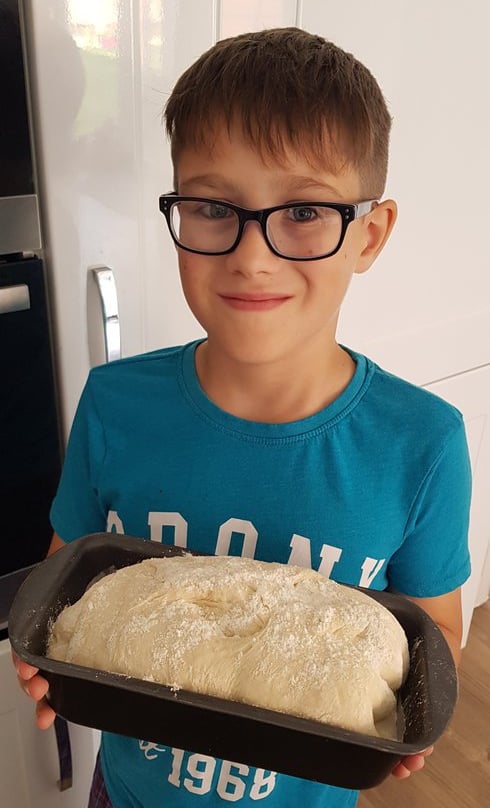 Young boy wearing glasses holding some bread ready to be put in the oven.