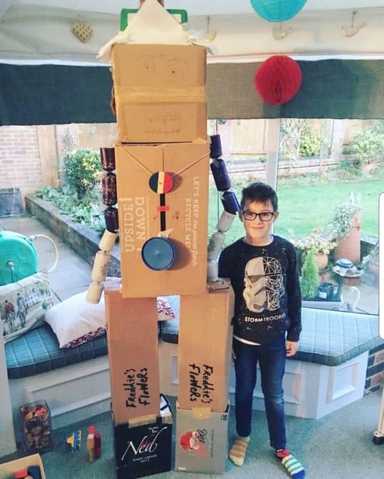 young boy standing next to a huge cardboard box robot.