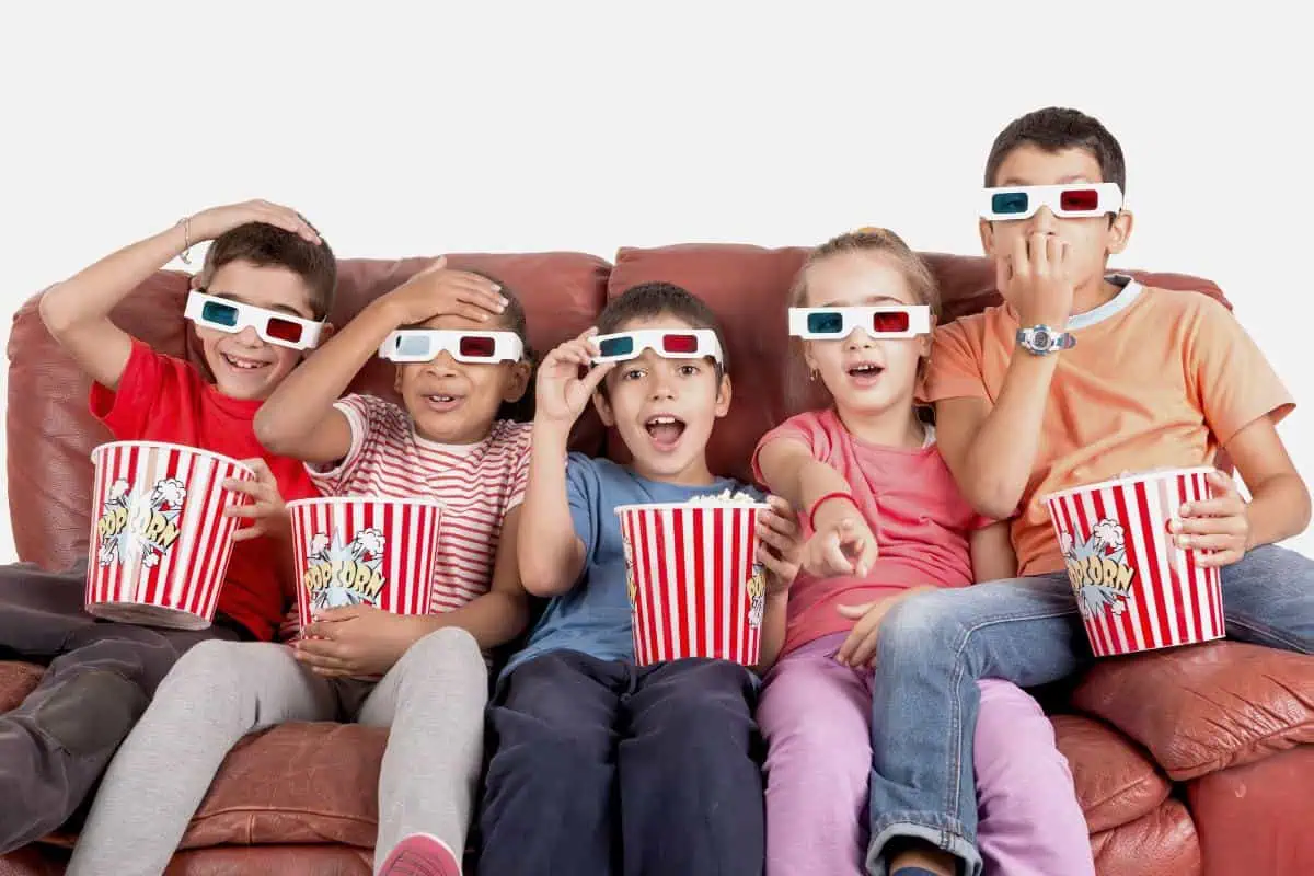 young children watching a movie wearing 3d glasses and eating popcorn