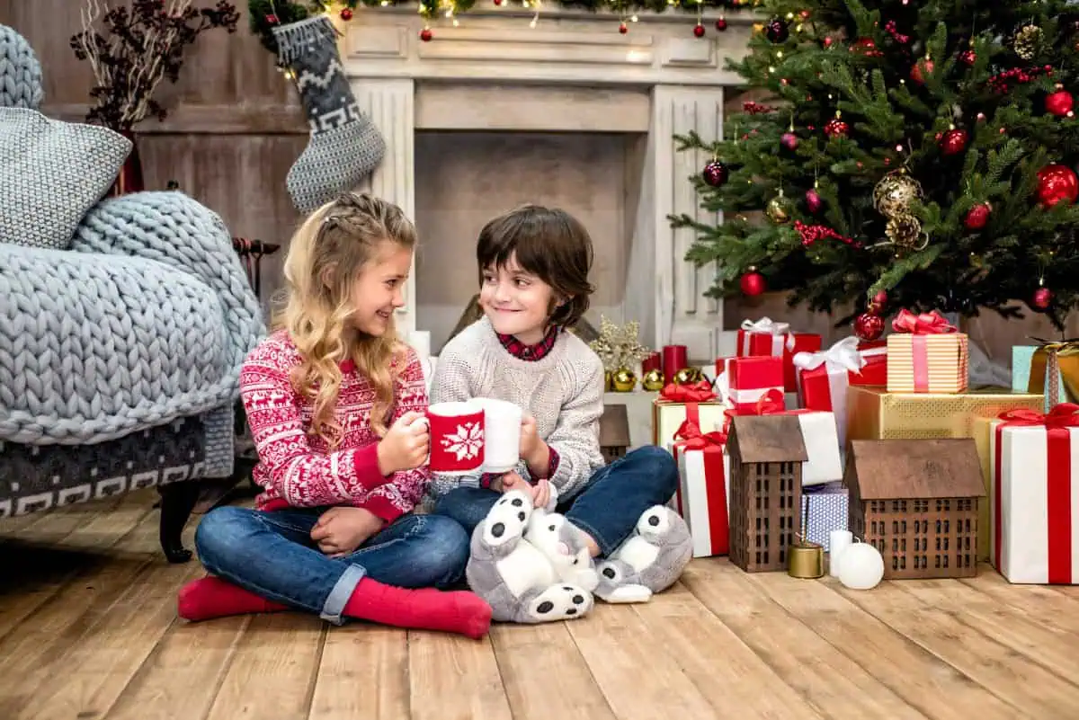 a young boy and a young girl sitting on the floor opening gifts