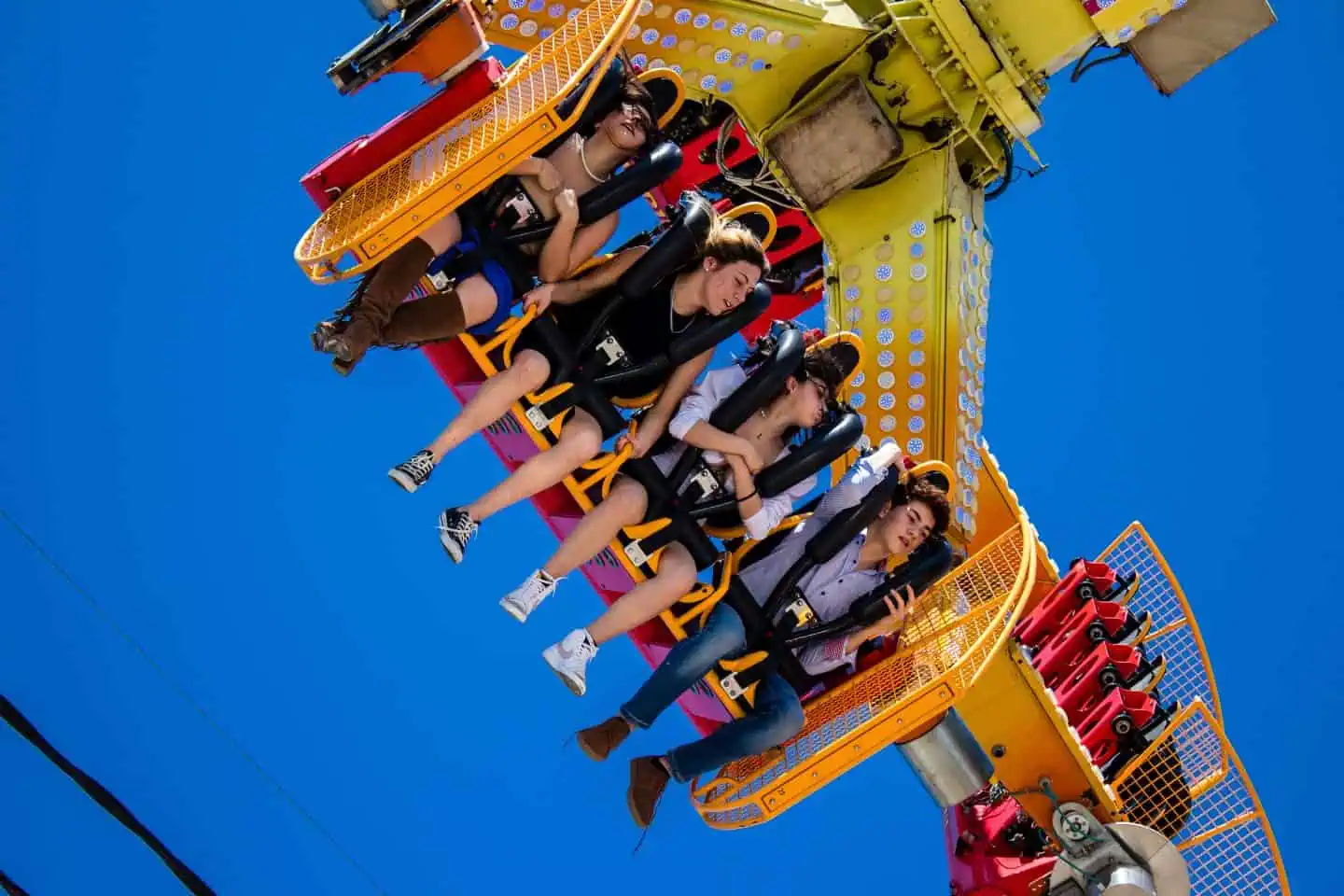 Five people strapped into seats on a brightly colored amusement park ride against a clear blue sky, experiencing an upside-down thrill.