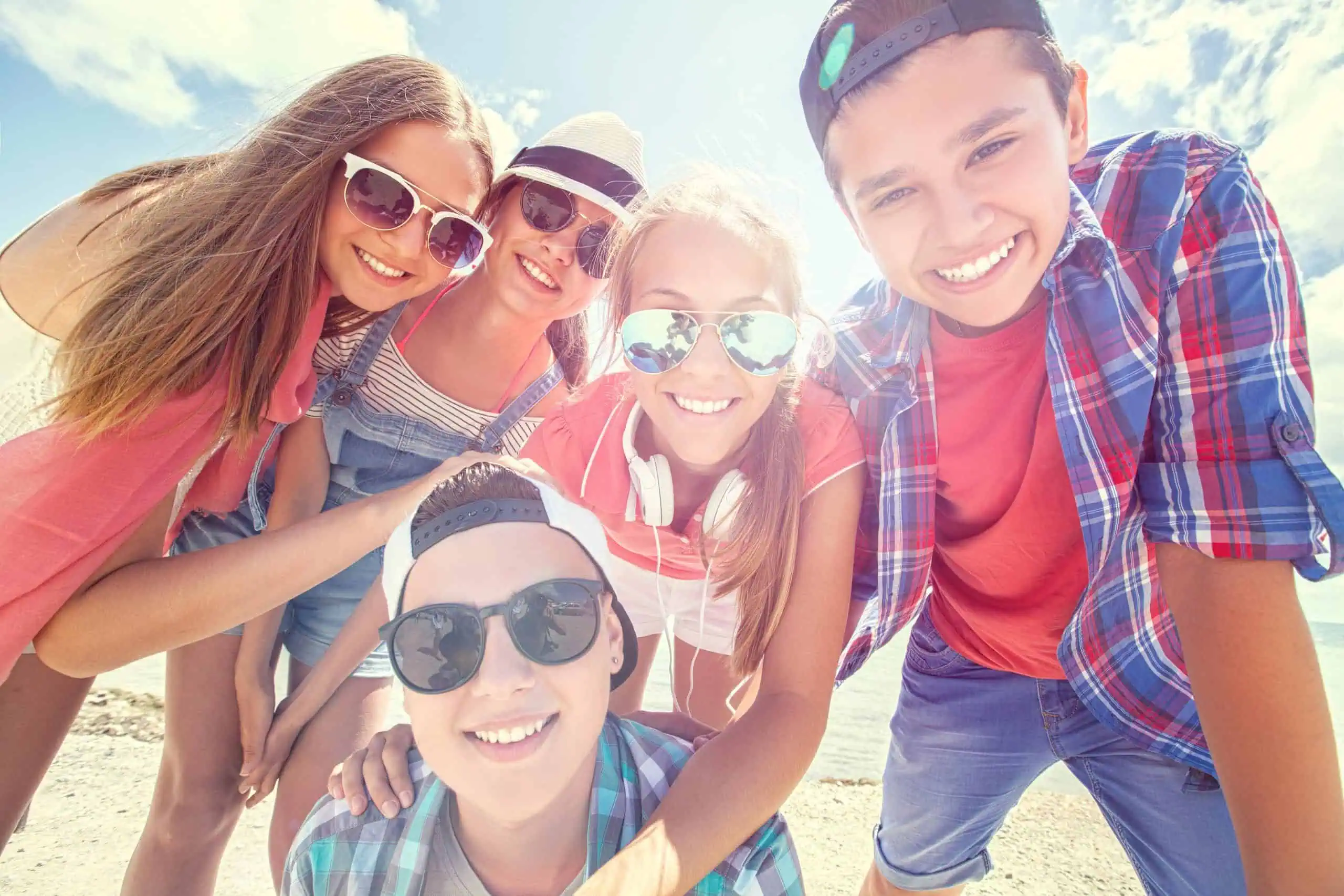 Group of teenagers smiling at the beach on a sunny day, perfect for a summer bucket list for teenagers