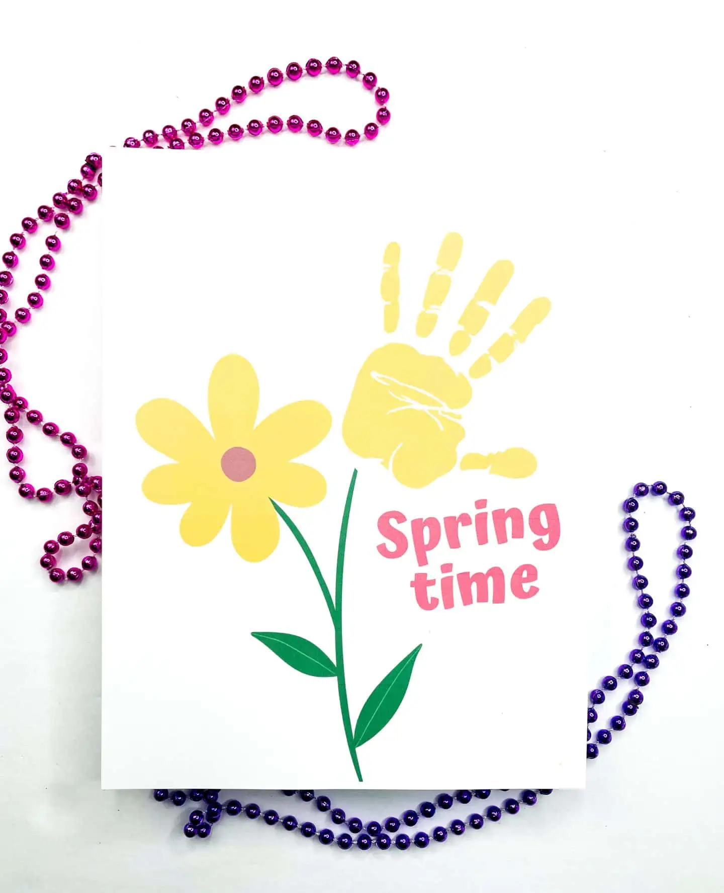 A cheerful handprint art printable with a yellow flower and child's handprint, featuring the words "Spring time" and surrounded by purple beads.

