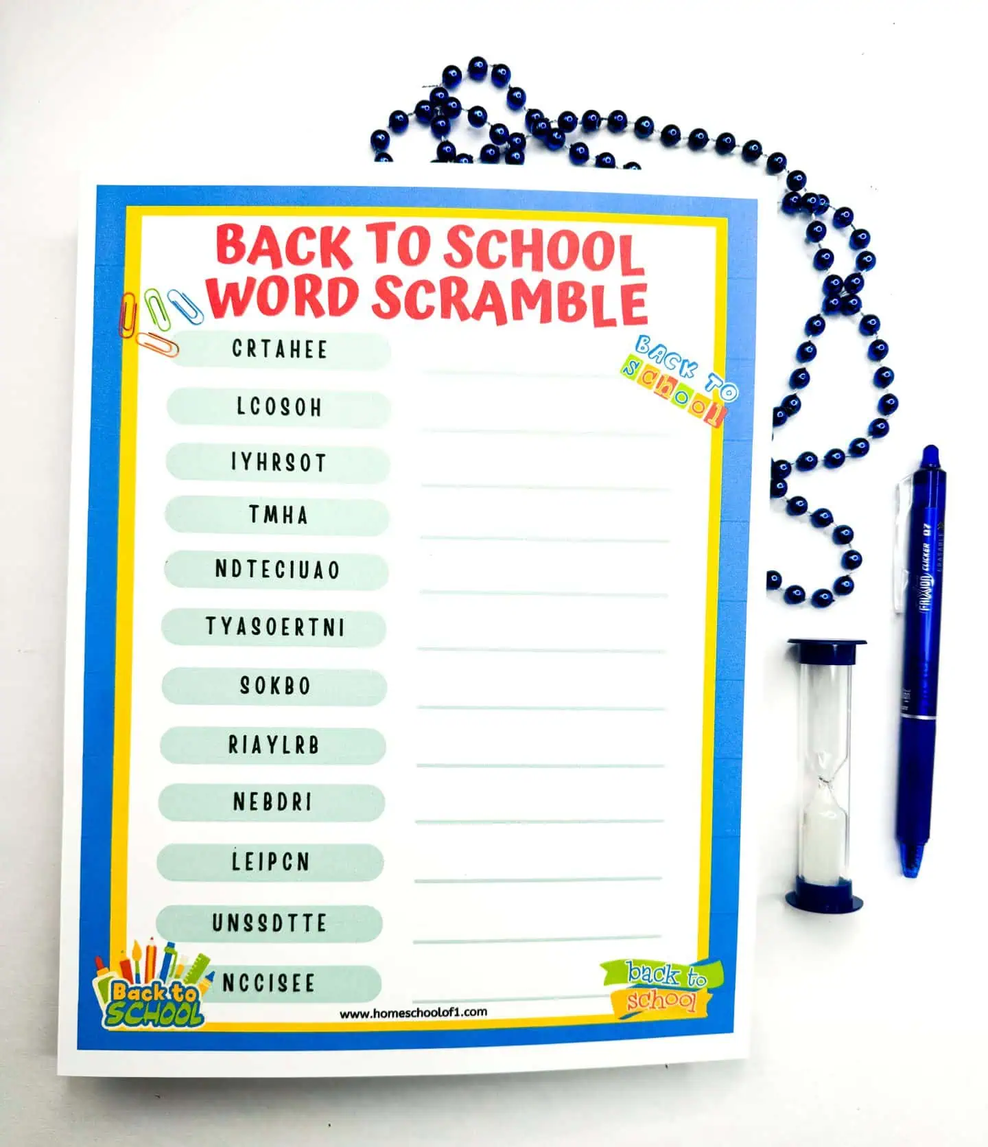 Back to School Word Scramble' worksheet placed on a white surface, with blue bead decorations forming a question mark and a blue pen to the right. The words to unscramble, like 'TEACHER' and 'CLASSROOM,' are listed on the left with blank spaces for answers.