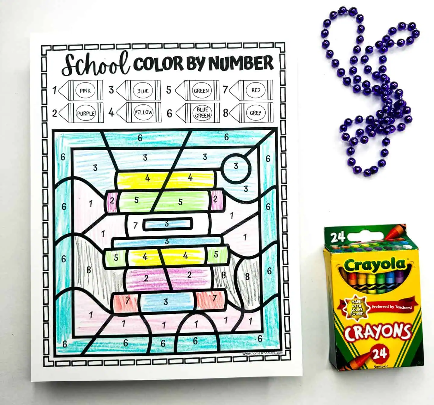 This worksheet contains a stack of books in a color by number format, each book colored as per the numerical guide. A bead design and a box of Crayola crayons suggest that this is part of a series of educational coloring activities.