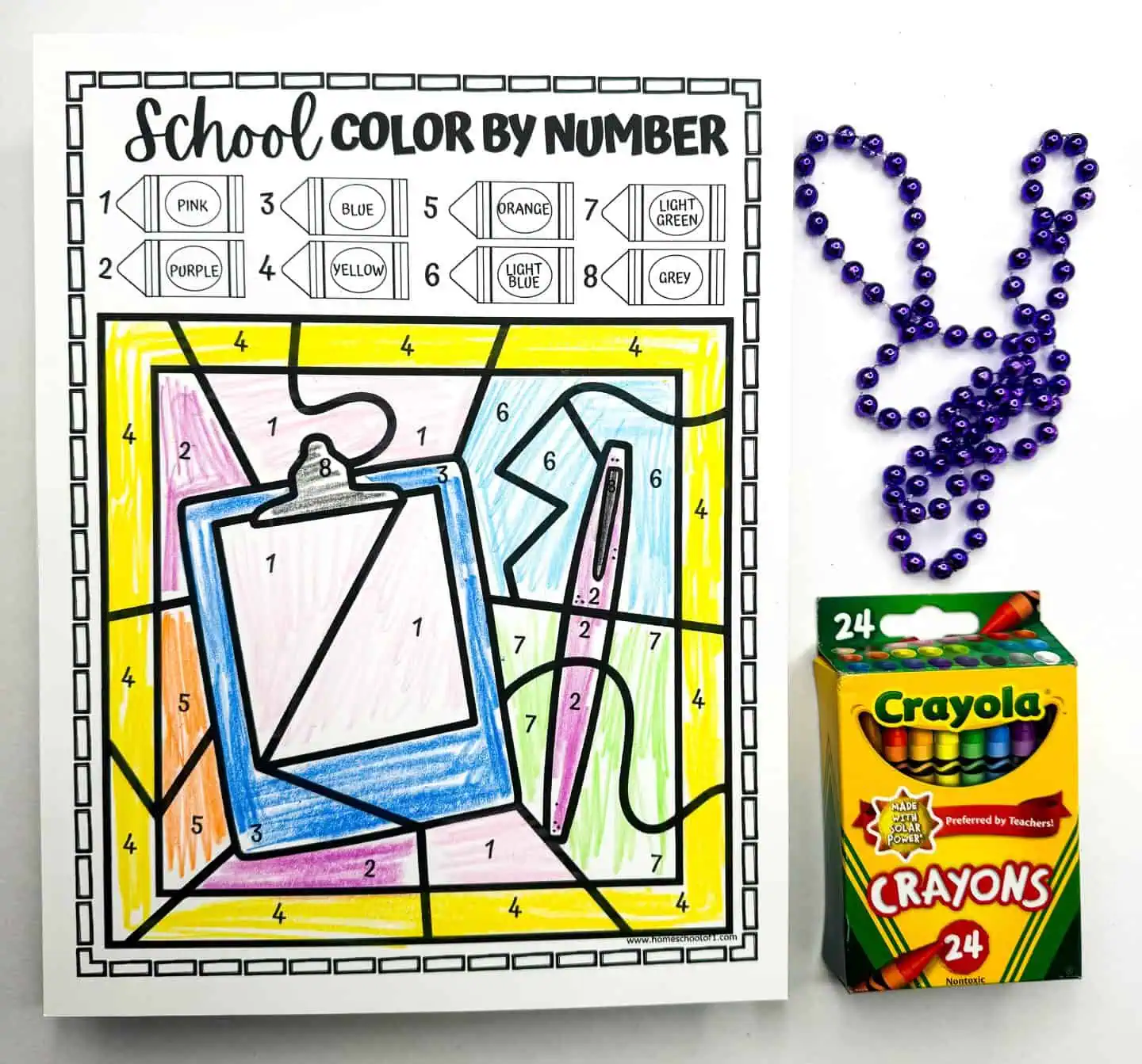 A creatively colored color by number worksheet depicts a clipboard and other stationery items, each section filled according to the color guide. The arrangement includes beads and a Crayola crayon box, enhancing the crafting theme.