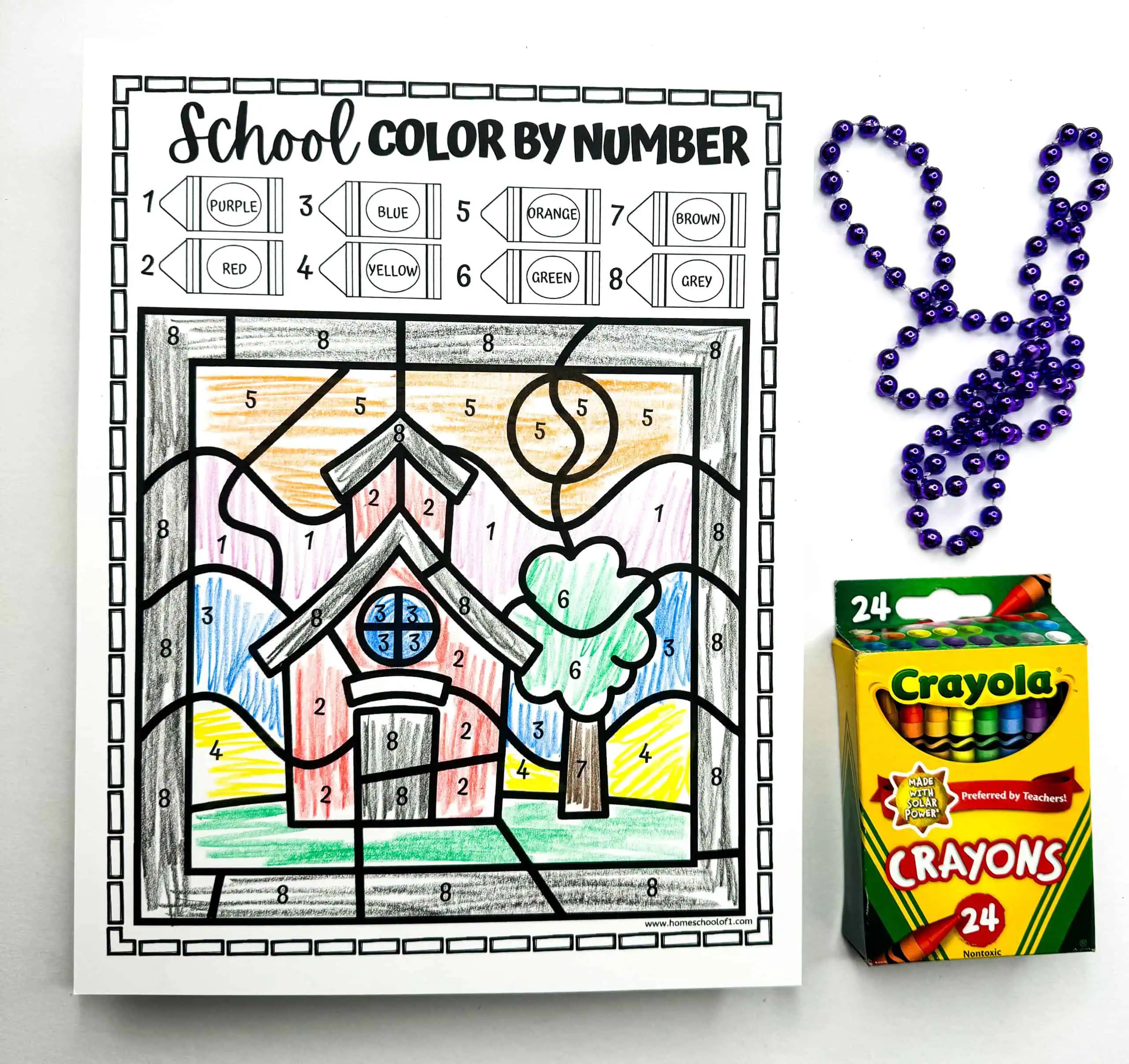 A school-themed color by number worksheet is partially colored in, showcasing a schoolhouse and tree. Beads and a Crayola crayon box are included, indicating a fun, educational coloring activity.