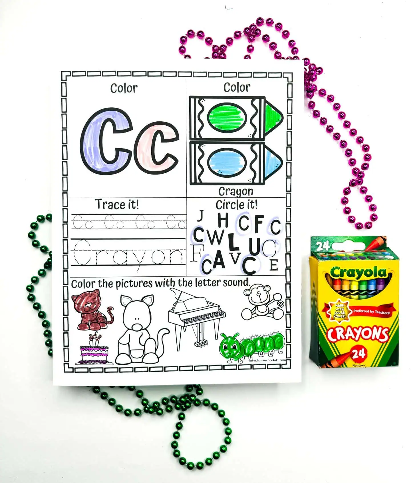 A learning activity sheet highlighting the letter C, including sections to color and trace the word "Crayon." It shows crayons and other objects starting with C like a cat and cake, colored in. The arrangement is complemented by green and purple beads and accompanied by a Crayola crayons pack.