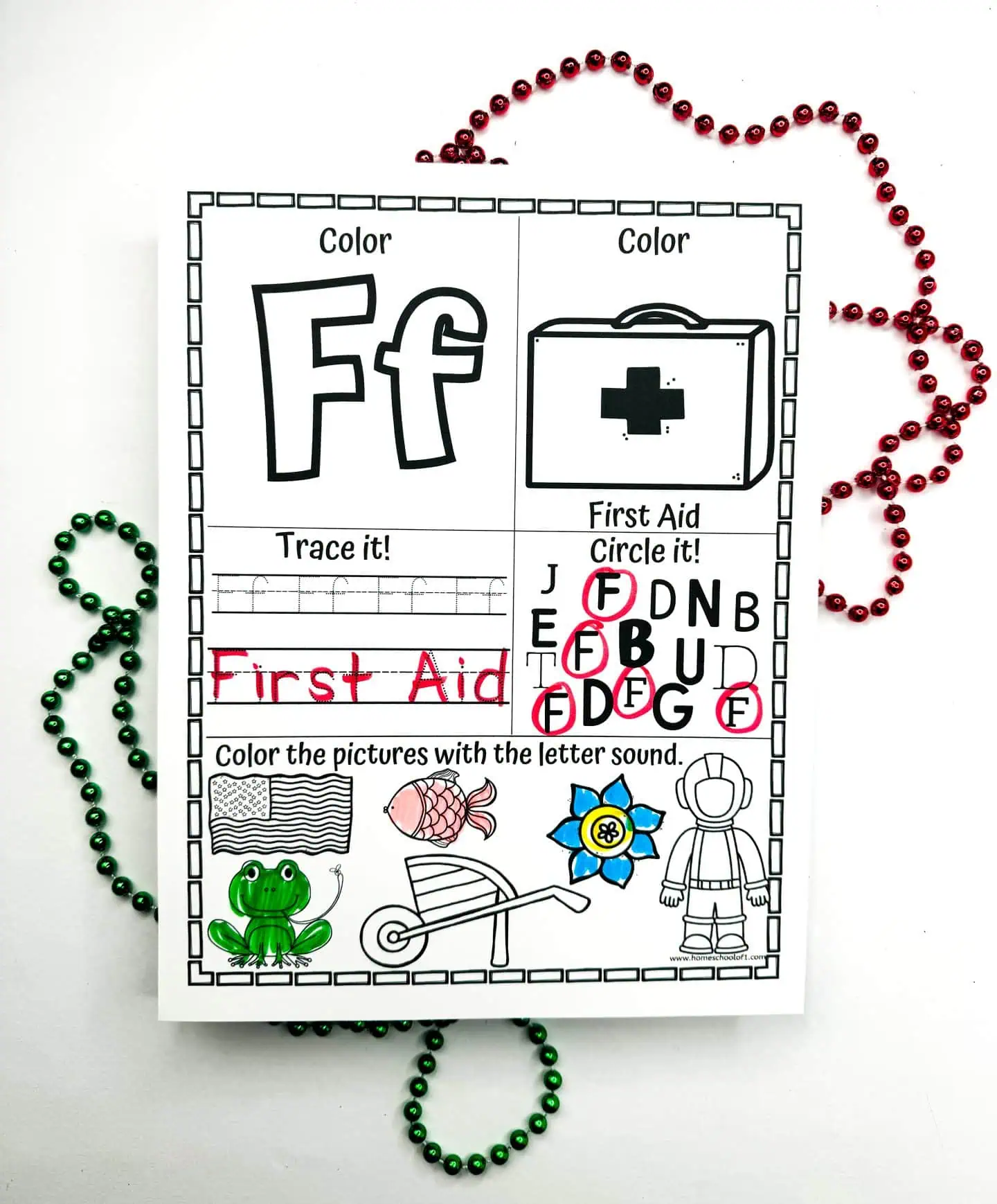 A worksheet for the letter F with activities like coloring and tracing the word "First Aid." It's adorned with images such as a frog, a flag, and a fish, which are all objects starting with F and have been partially colored in. The aesthetic layout includes red and green beads spiraling around, while a box of Crayola crayons adds a touch of practicality to the scene.






