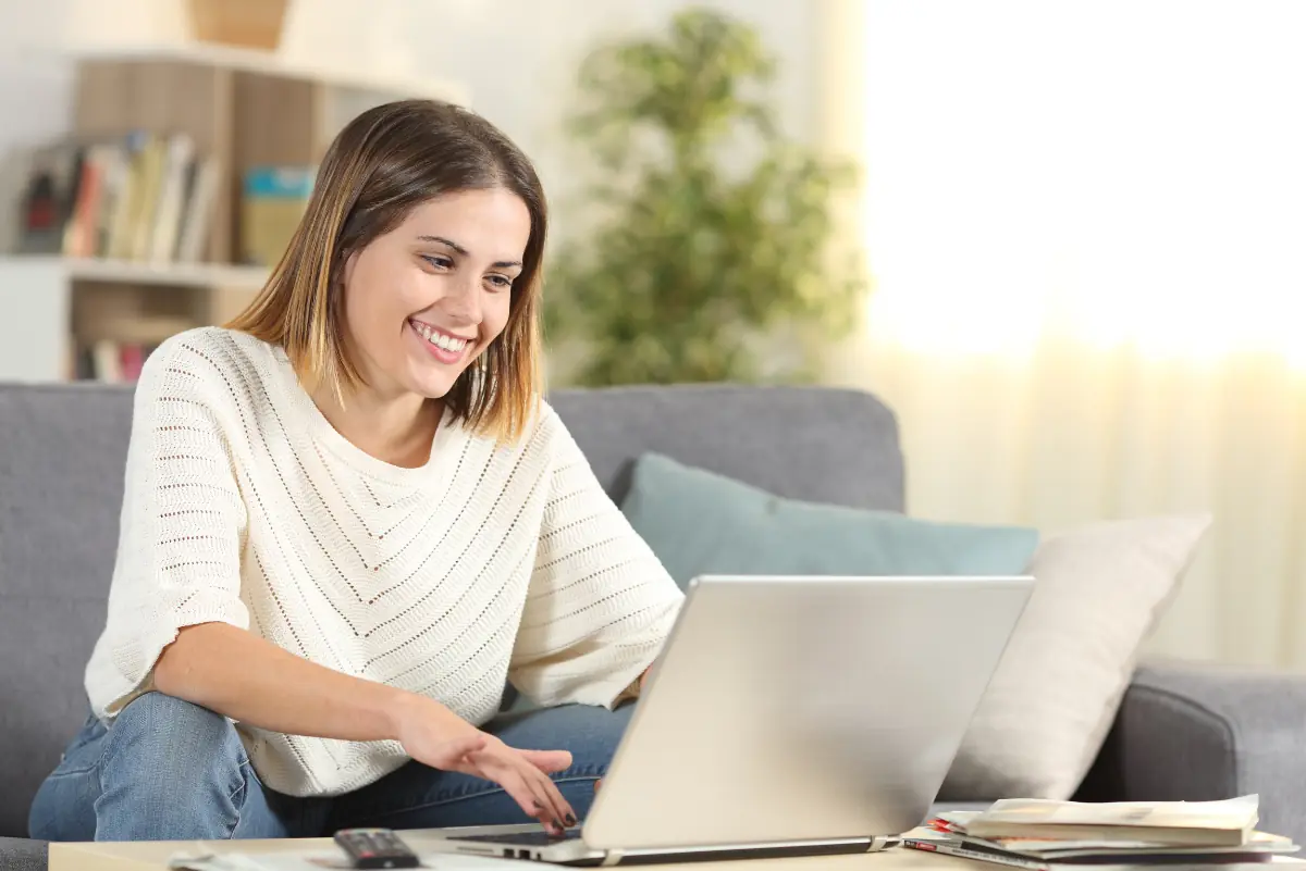 Happy homeschool mom checking laptop online content sitting on a couch in the living room at home