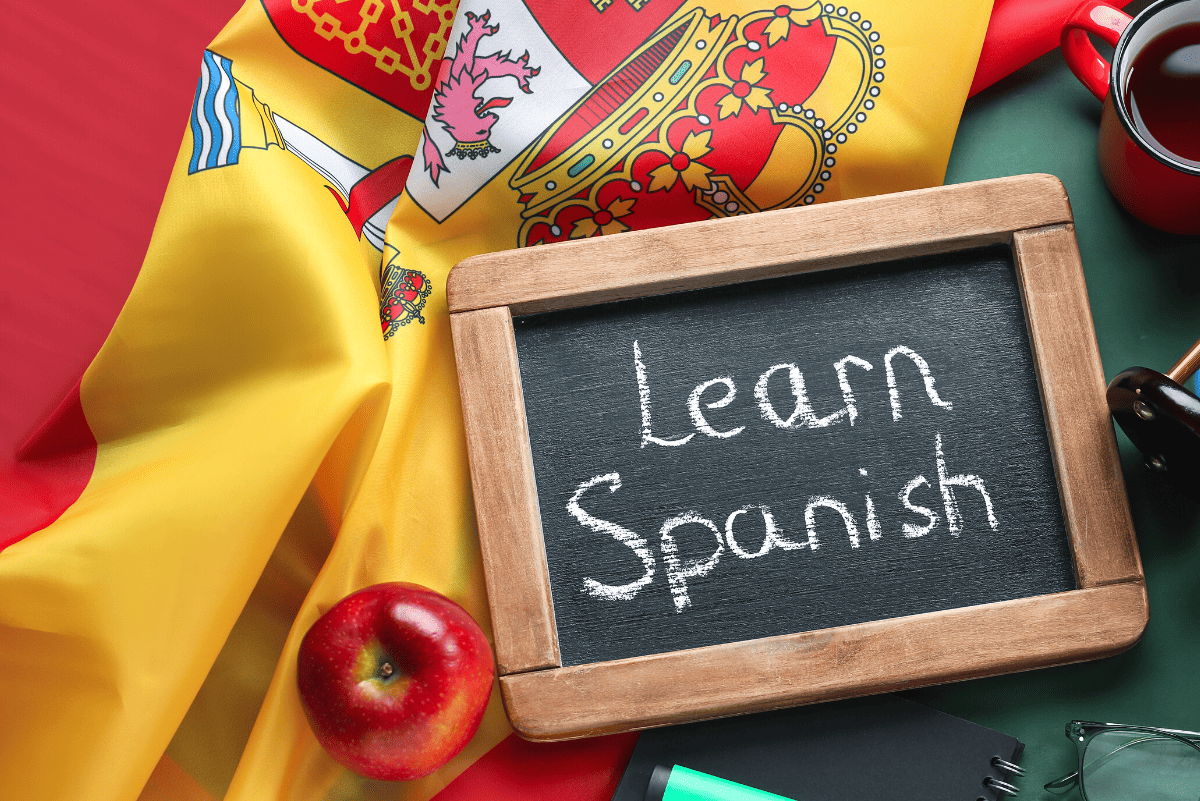 Learn Spanish concept with a small chalkboard on a vibrant Spanish flag, an apple, and a cup of coffee, symbolizing engaging homeschool Spanish curriculum materials.