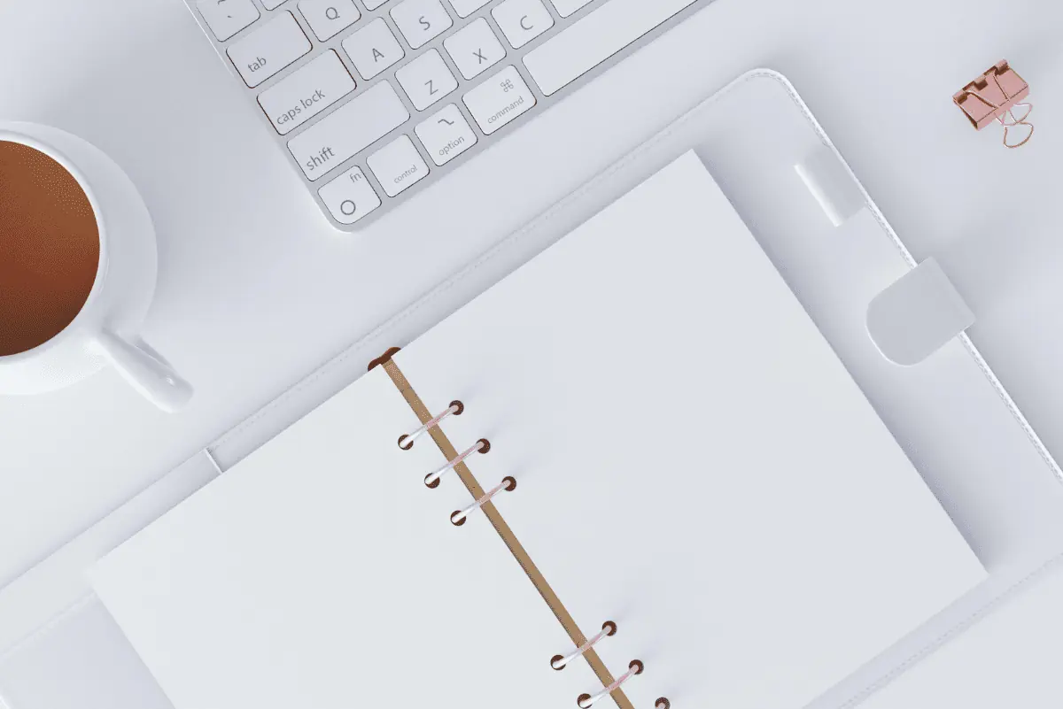 A minimalist homeschooling setup with a cup of coffee, white keyboard, and an open blank lesson planner, embodying the simplicity and efficiency of the best homeschool lesson planner.