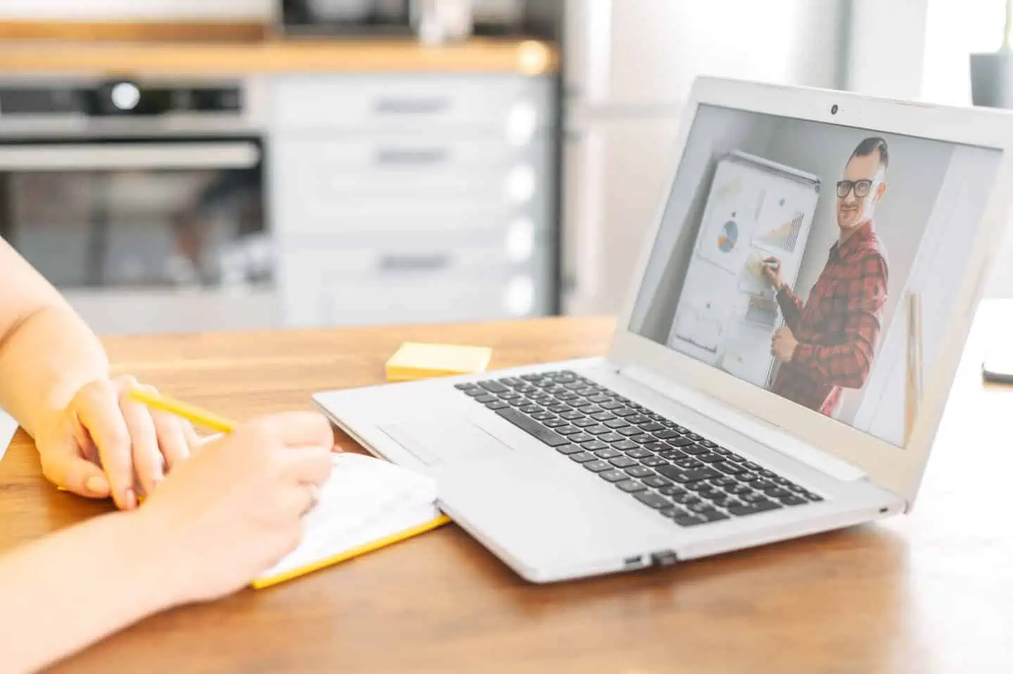 Female hands is writing in notebook while male teacher, tutor, coach on the laptop conducts online training, webinar. Online learning concept