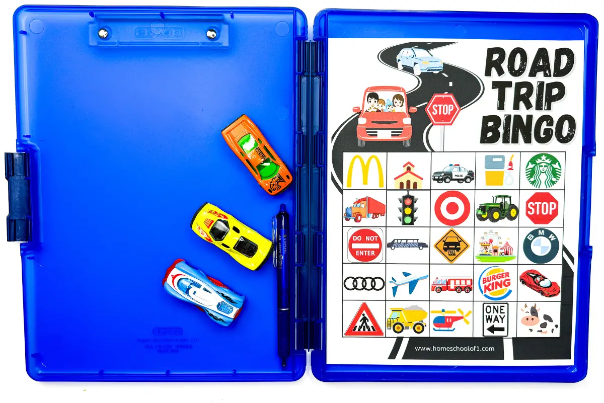 Close-up of a 'Road Trip Bingo Printable' inside a blue folder, with miniature cars alongside, creating a perfect game for kids to stay entertained on long drives.