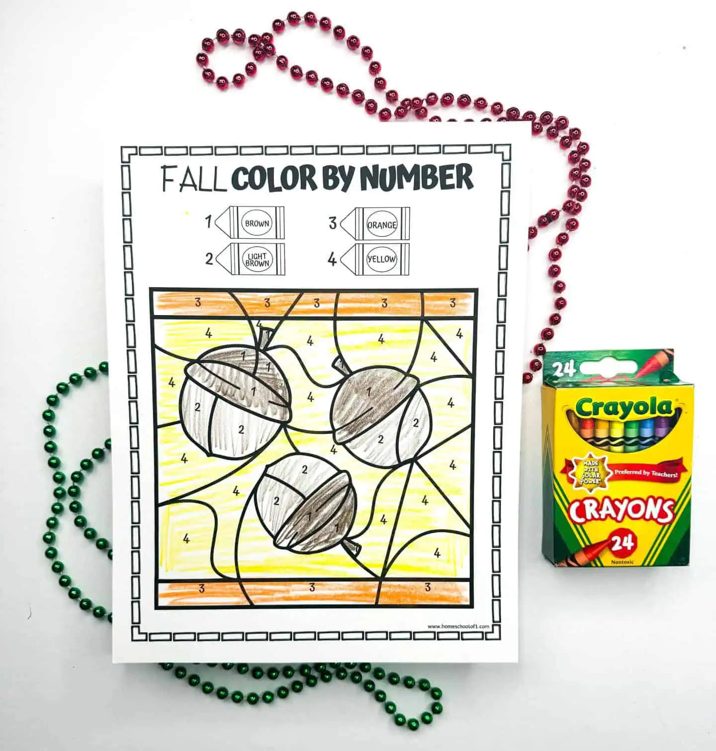 A fall-themed color by number printable with acorns ready to be colored, flanked by festive bead necklaces and a Crayola crayon pack.