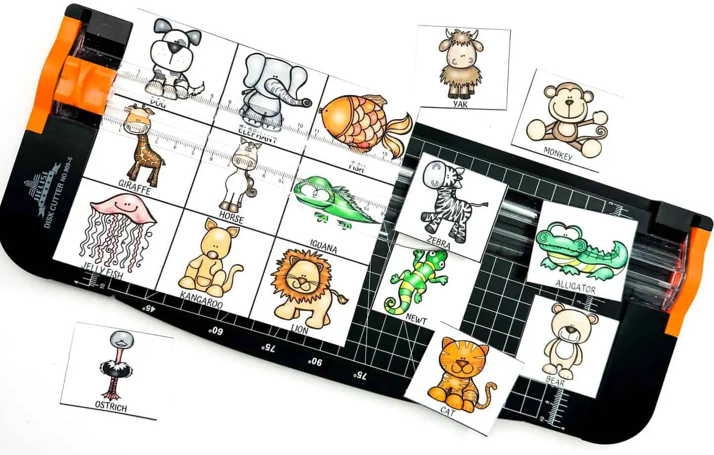 Various animal cartoon cards including a jellyfish, giraffe, and alligator organized on a paper cutter alongside measuring grids