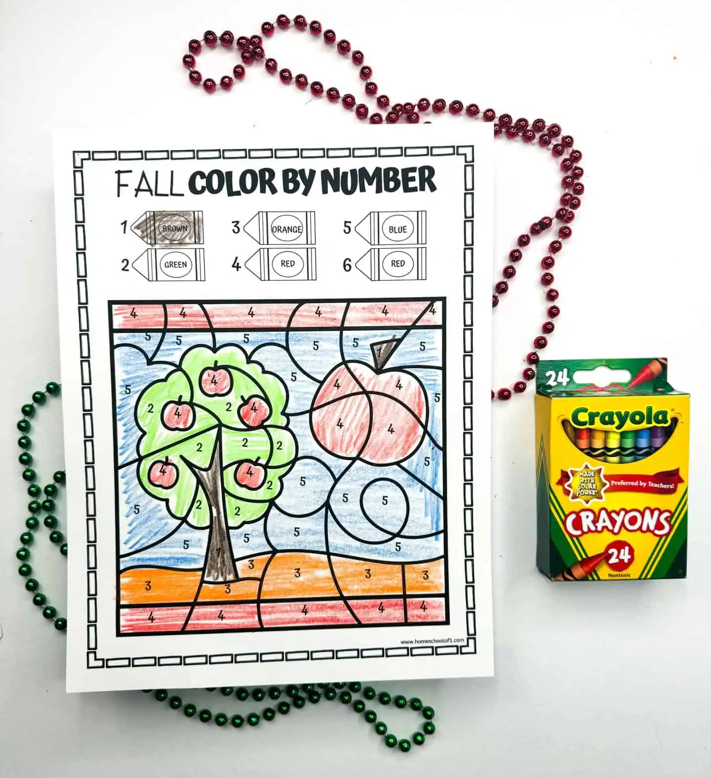 Color by number activity page with an apple tree and a red apple, alongside a box of Crayola crayons and bead necklaces.