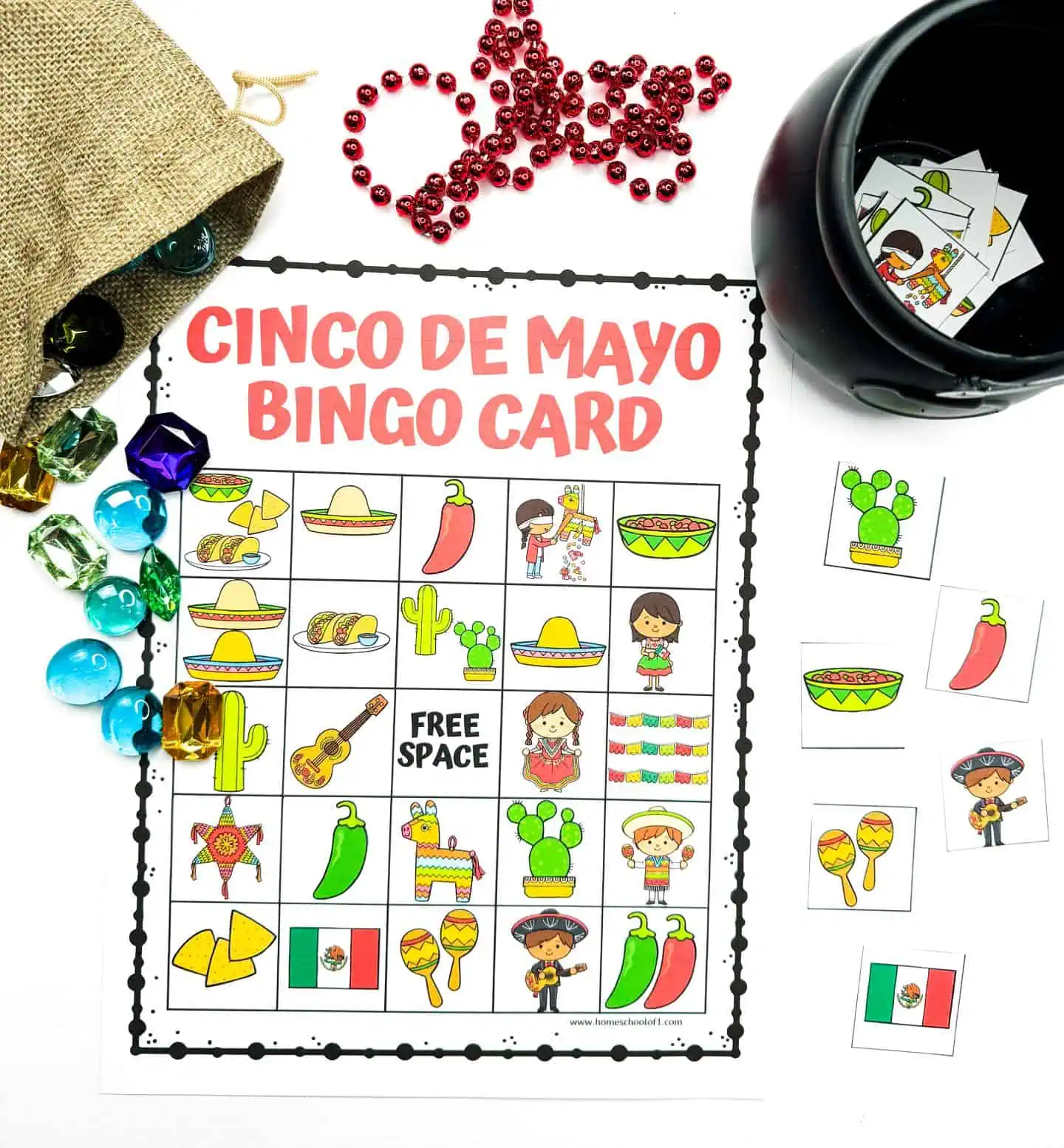 A vibrant 'Cinco de Mayo Bingo Card' surrounded by festive accessories including red beads, a burlap sack spilling out colorful game pieces, and a black pot filled with bingo cards, all arranged on a white background