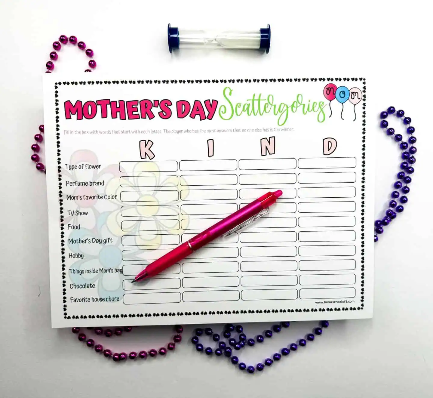 A Mother's Day Scattergories activity sheet with the word 'KIND' highlighted across the top. It's adorned with a pink pen and colorful beads, and includes categories like 'Type of flower' and 'Mother's Day gift'