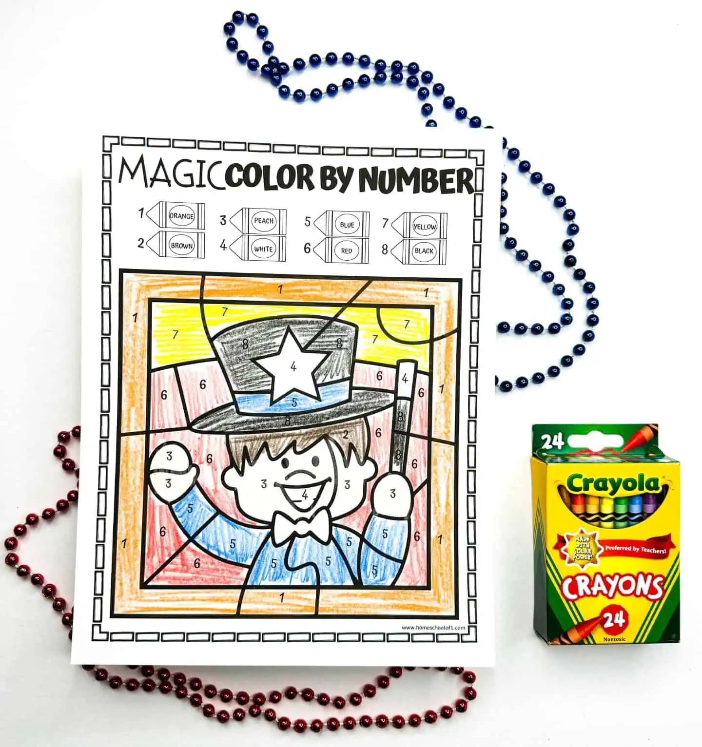 Colored worksheet of a smiling magician in a top hat with a star, displayed alongside decorative beads and a box of 24 Crayola crayons.