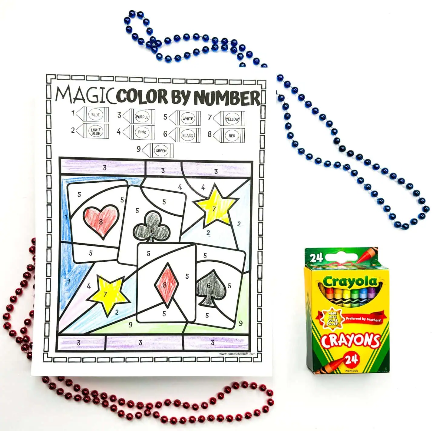 "Worksheet colored by numbers presenting playing card symbols in abstract shapes, decorated with beads and a box of crayons to the side