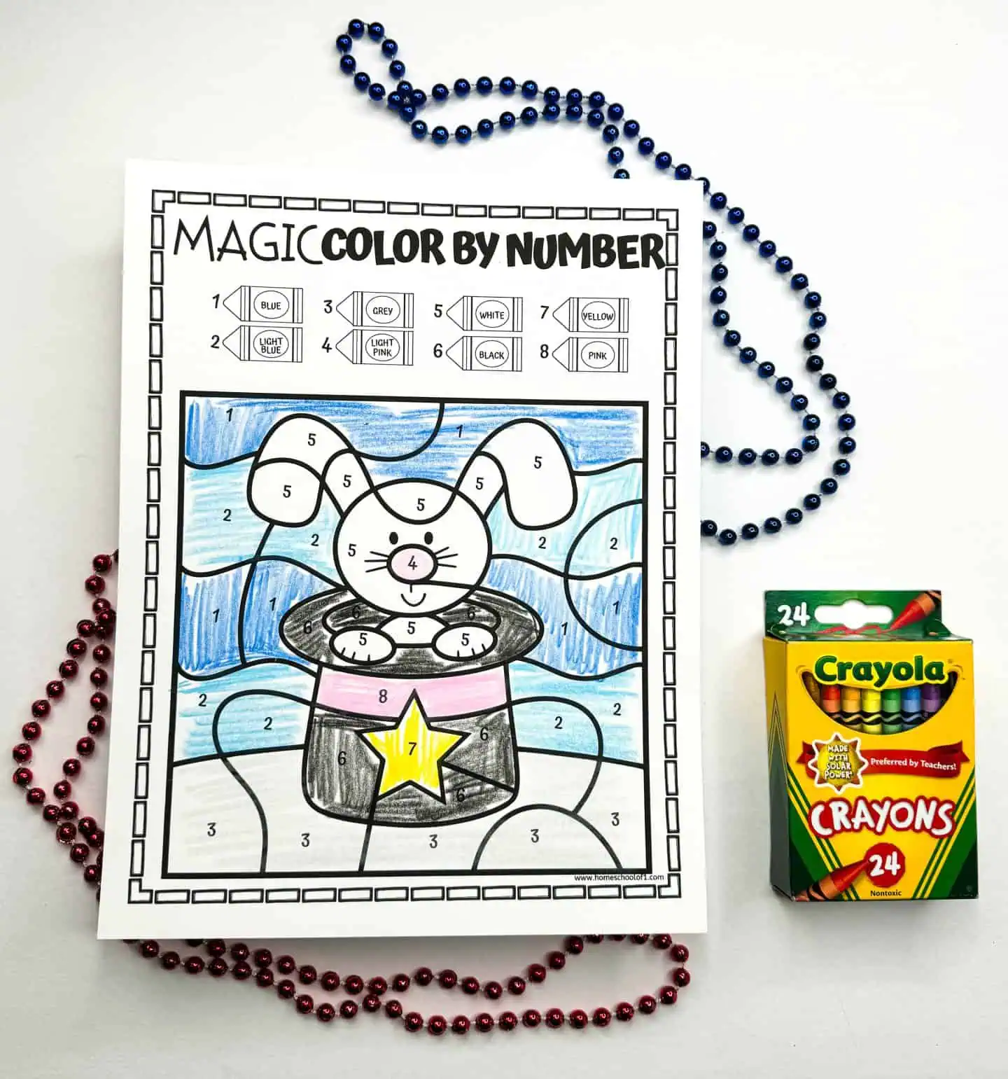 A completed color by number sheet with a rabbit in a magician's hat, flanked by bead necklaces and a Crayola crayons box.