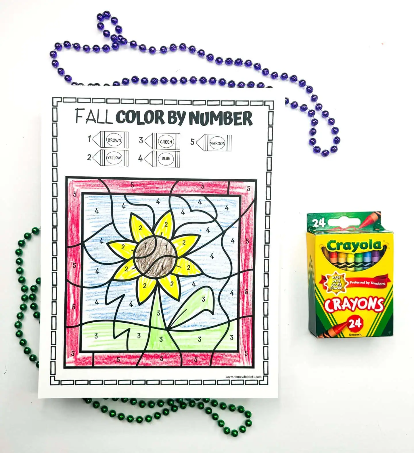 Worksheet for coloring a sunflower by number, adorned with a backdrop of bead necklaces and a Crayola crayons pack.