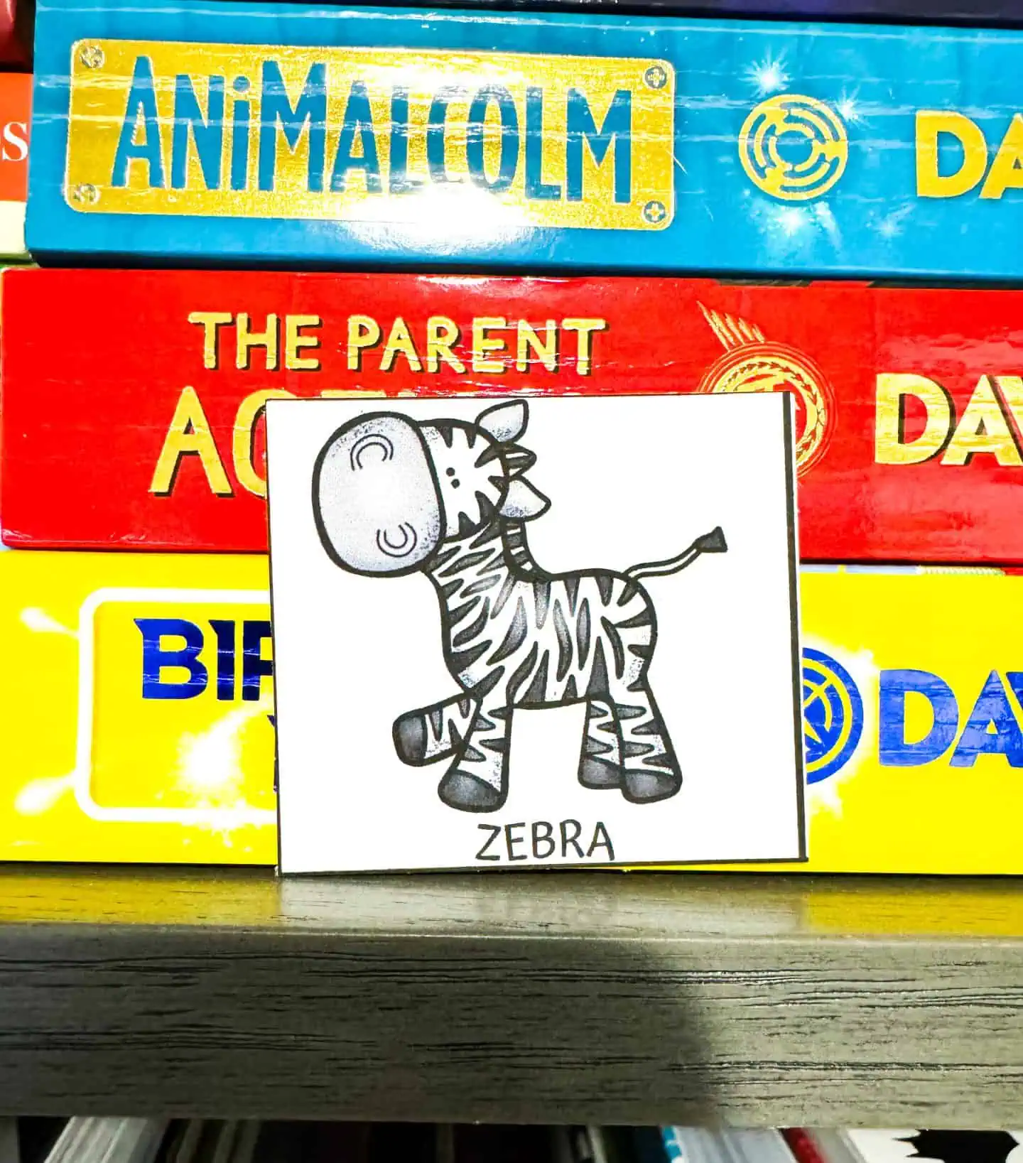 A playful cartoon zebra card labeled 'ZEBRA' placed against a stack of colorful children’s books