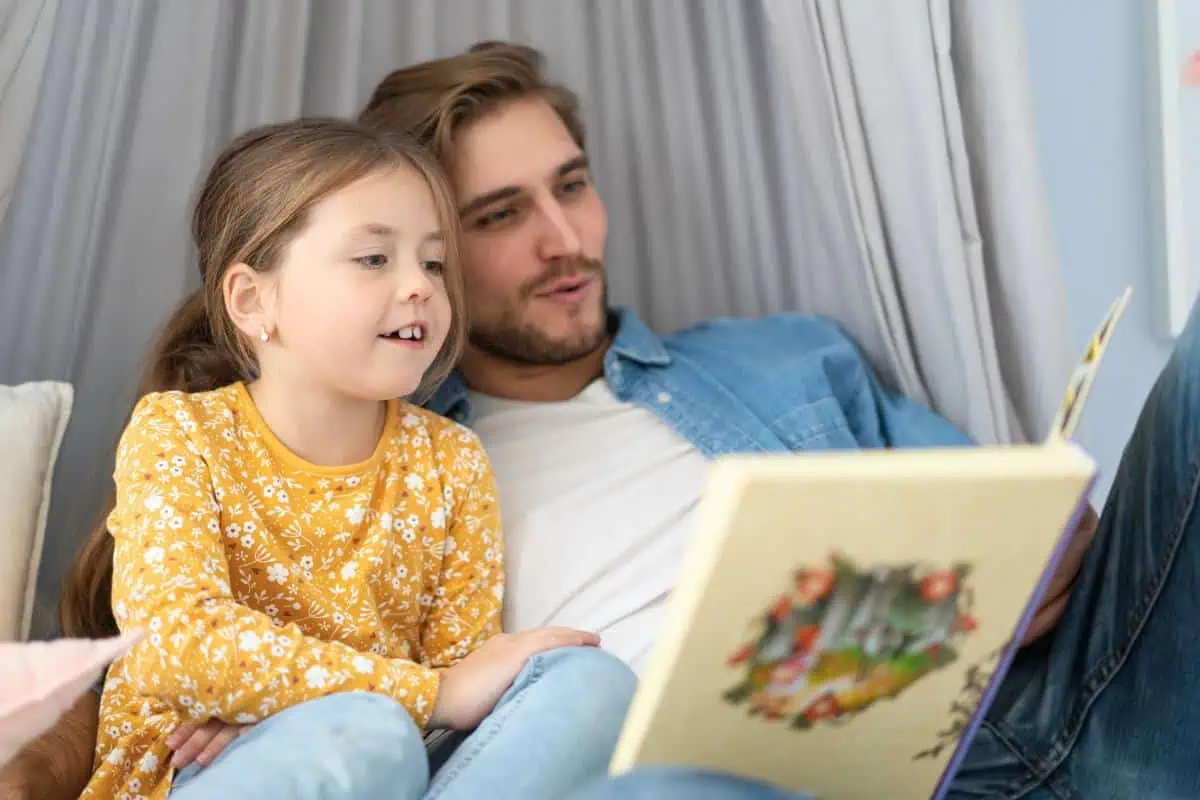 A father and his daughter are sharing a book while sitting in a cozy reading nook. A great moment for bonding over stories on Father's Day.