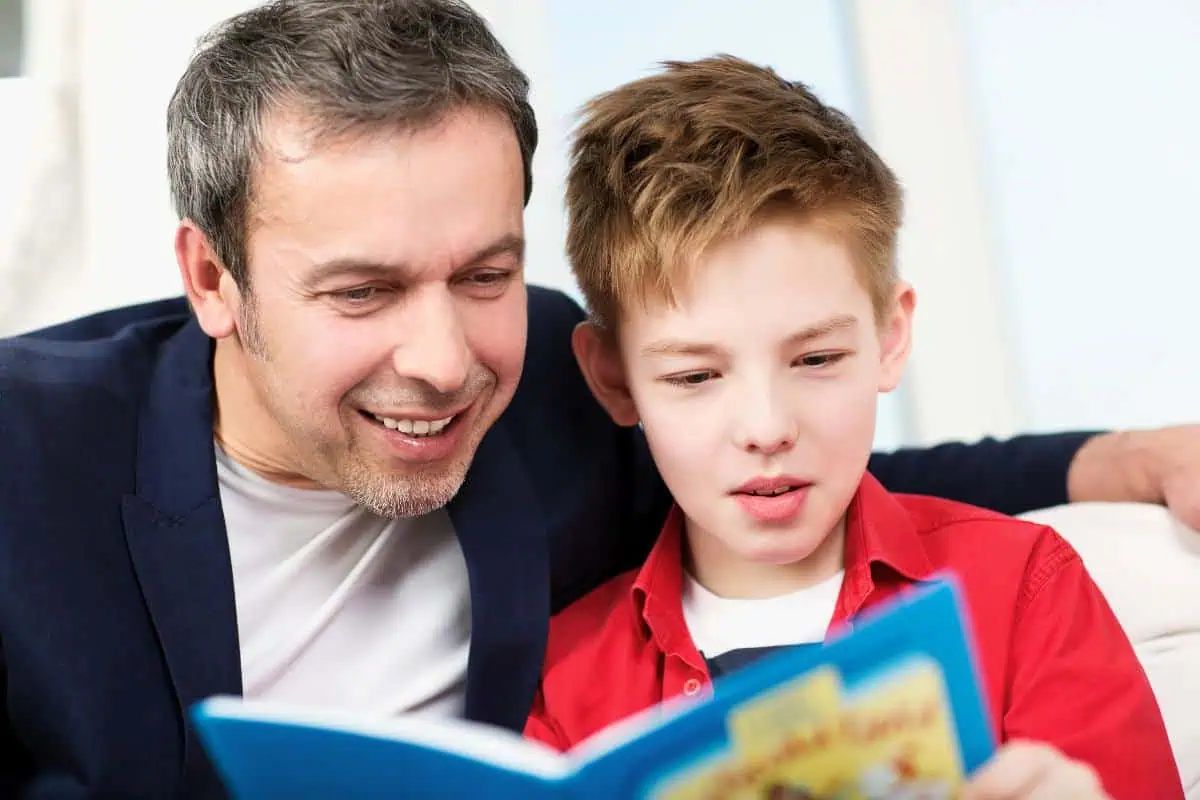 A father and his young son are reading a book together on a couch, enjoying quality time. Perfect for celebrating Father's Day with books for kids.