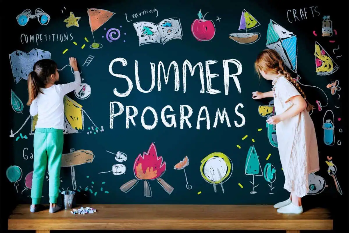 Two girls drawing on a chalkboard with the words 'Summer Programs' surrounded by colorful drawings of campfires, boats, and crafts, highlighting summer learning activities.