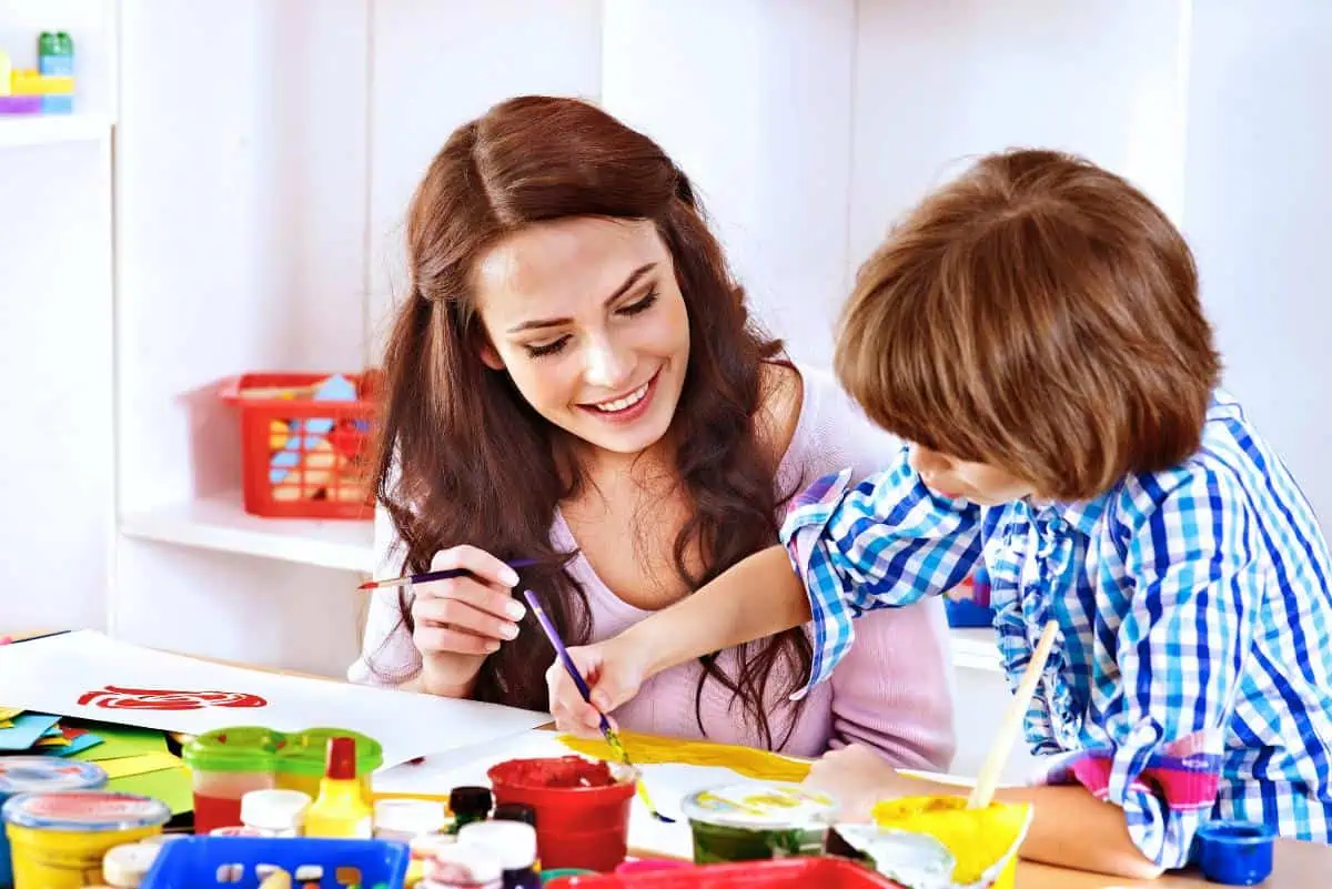 A smiling woman and a child painting together at a table filled with colorful art supplies, illustrating creative homeschooling tips