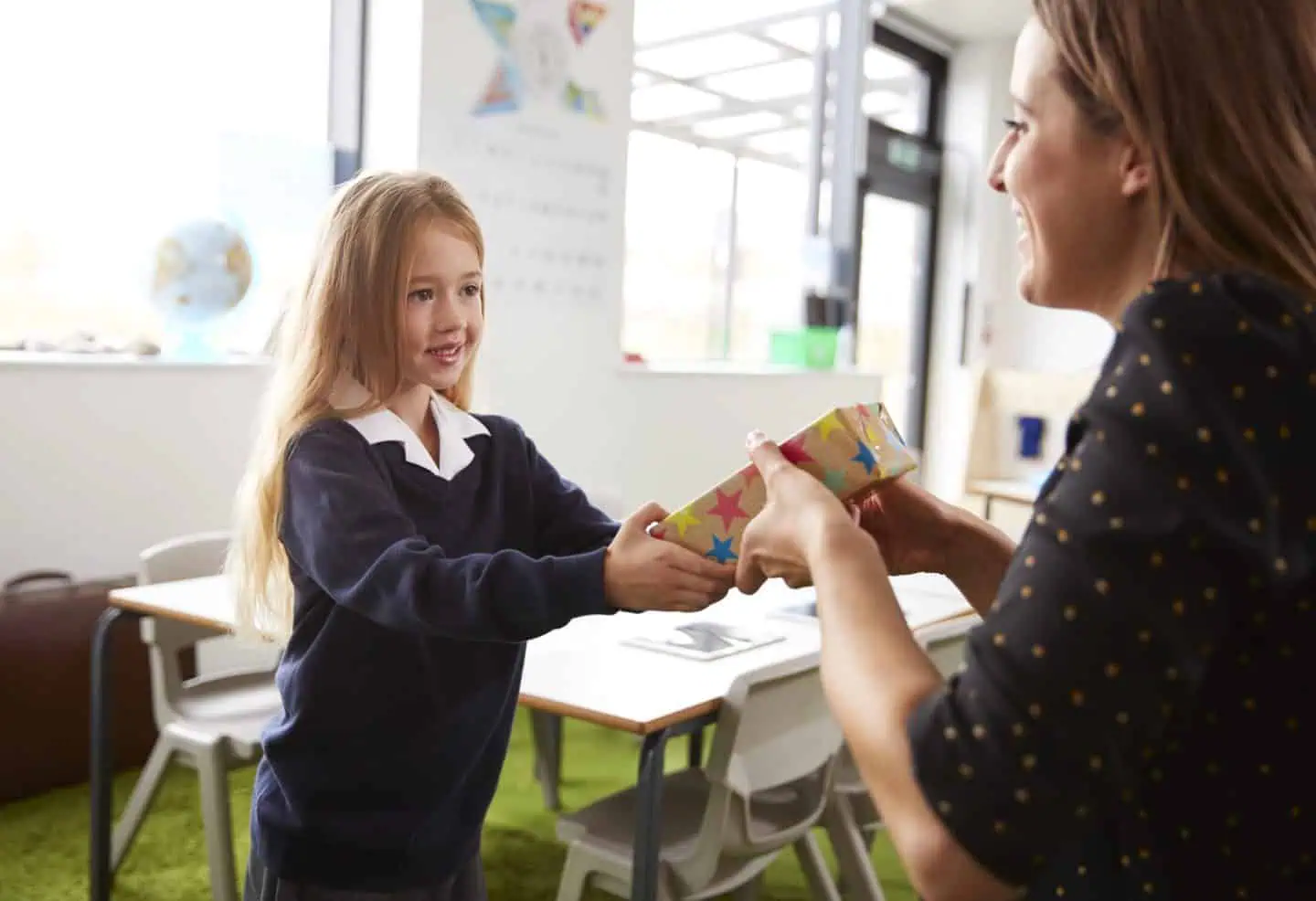 young girl giving her female teacher a gift on the first day of school